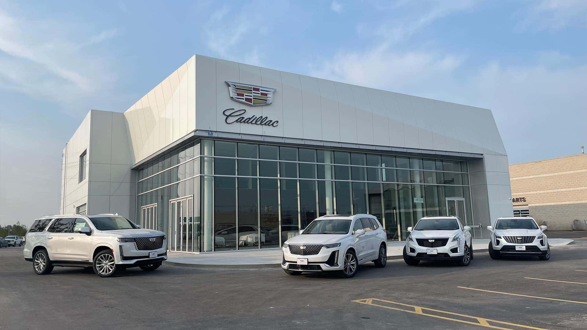 Cadillac dealership with four white SUVs parked outside under a clear sky.