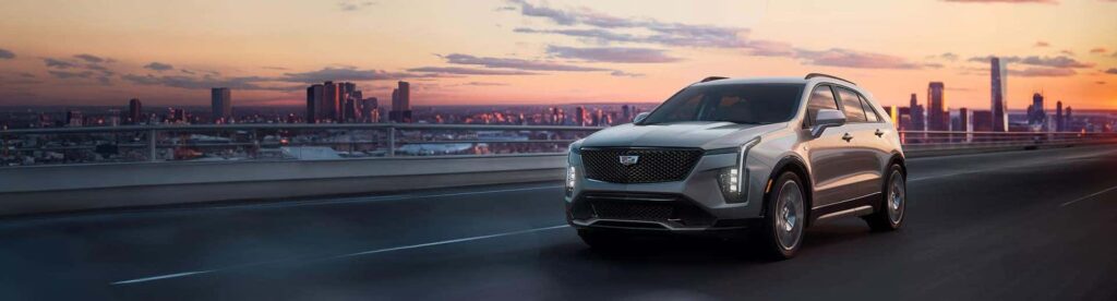 Silver SUV driving on a highway with a city skyline at sunset in the background.