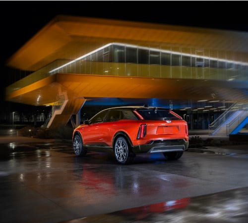 Red SUV parked outside a modern, illuminated building at night.