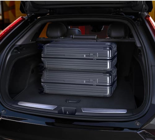 Two silver suitcases stacked in the open trunk of a black SUV.