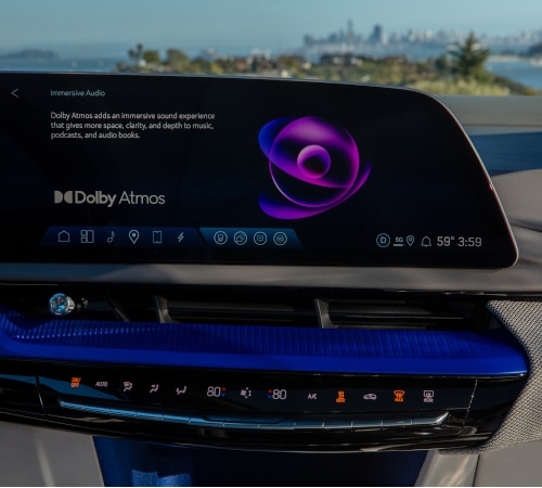 Car dashboard with Dolby Atmos display, audio controls, and cityscape in the background.
