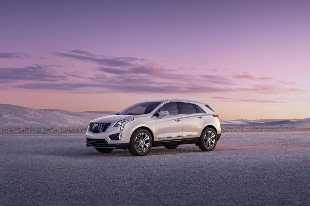 Silver SUV parked on a desert landscape during a vibrant pink and purple sunset.